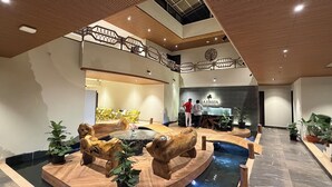 Una hall d'albergo con un'area salotto centrale in legno, una reception e una piscina con sculture in legno.
