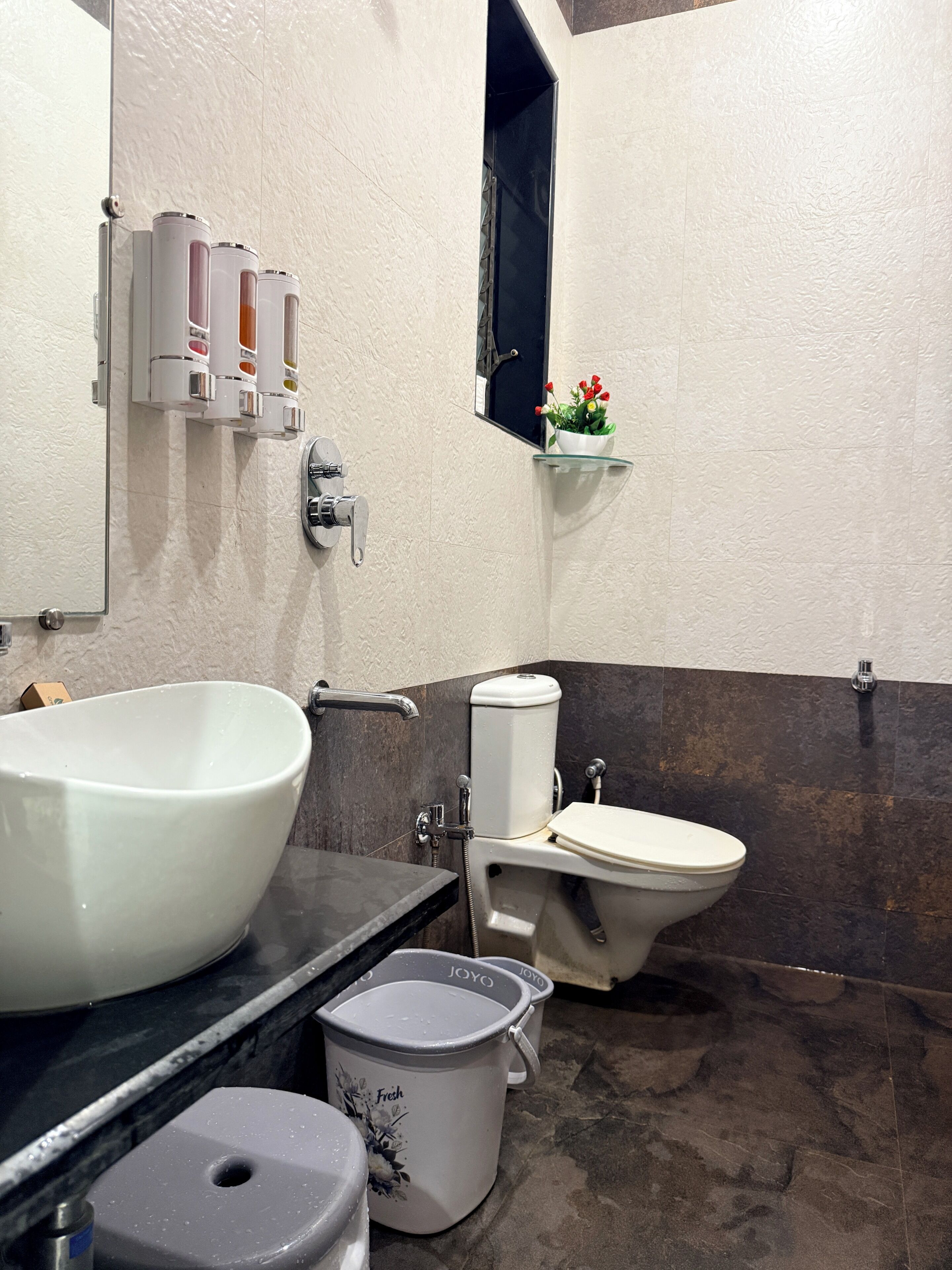 Un baño con un lavamanos grande y blanco, un inodoro, una ducha y un pequeño estante con flores.