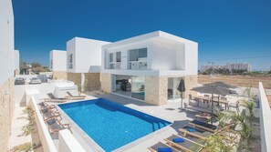 Une maison moderne à deux étages, dotée d’une piscine, d’un espace extérieur aménagé et offrant une vue sur les environs.