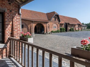 A brick building with arched doorways, a cobblestone courtyard, and a wooden balcony railing.