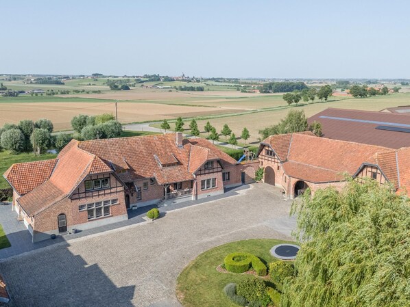 A large, traditional brick building with multiple wings, a central courtyard, and a surrounding landscape.