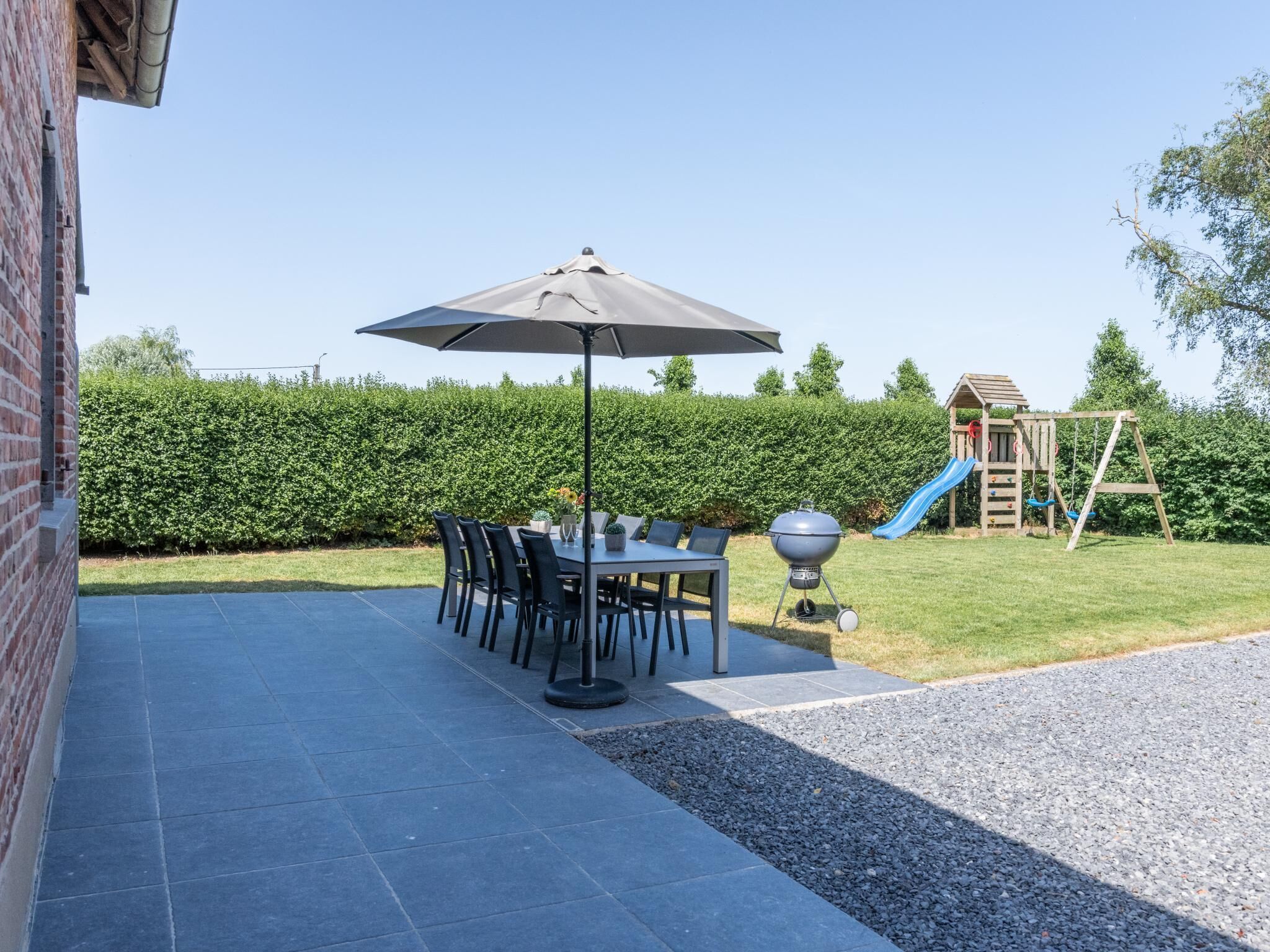 En terrasse med et bord, stole, grill og en legeplads for børn.