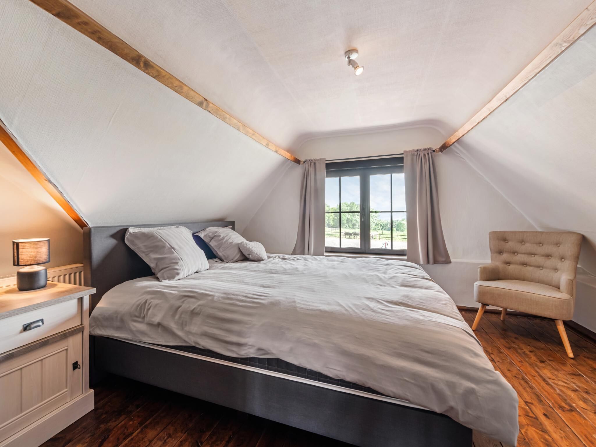 A bedroom with a bed, a nightstand, a chair, a window, and a sloped ceiling.