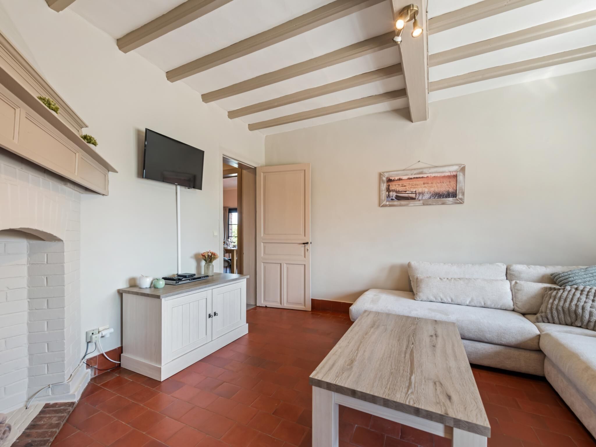 Un salon avec une cheminée, un téléviseur fixé au mur, un canapé et une table en bois.