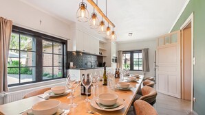A modern kitchen with a long dining table set for six, large windows, and a view of the outside.