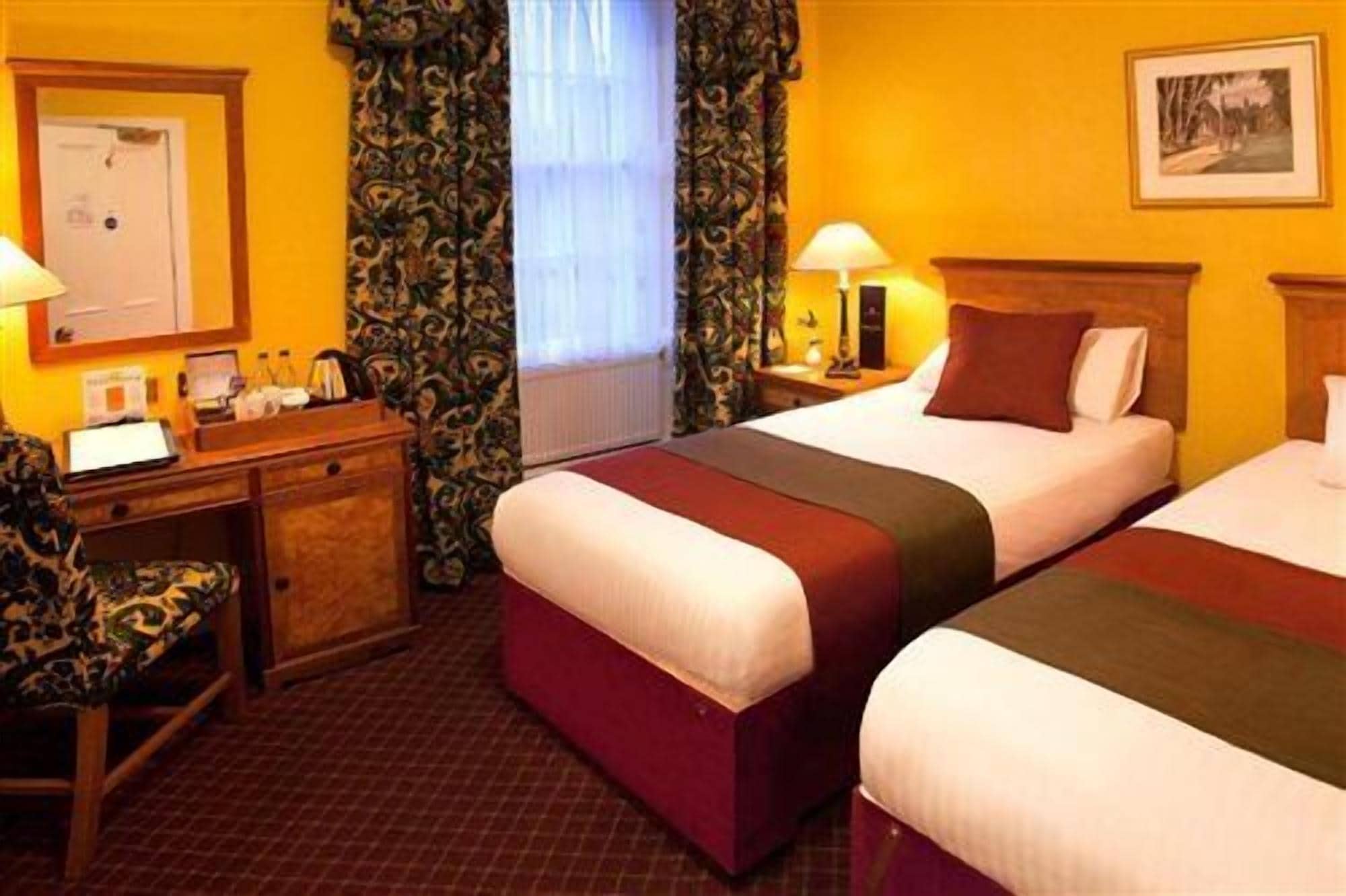 Una habitación de hotel con dos camas, un escritorio, una silla y una ventana con cortinas.