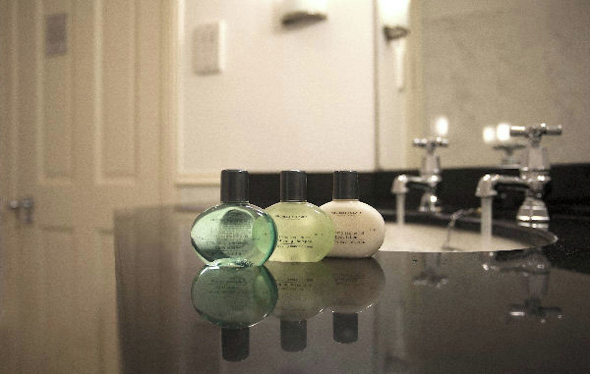 A bathroom counter with three bottles of liquid soap and a mirror.