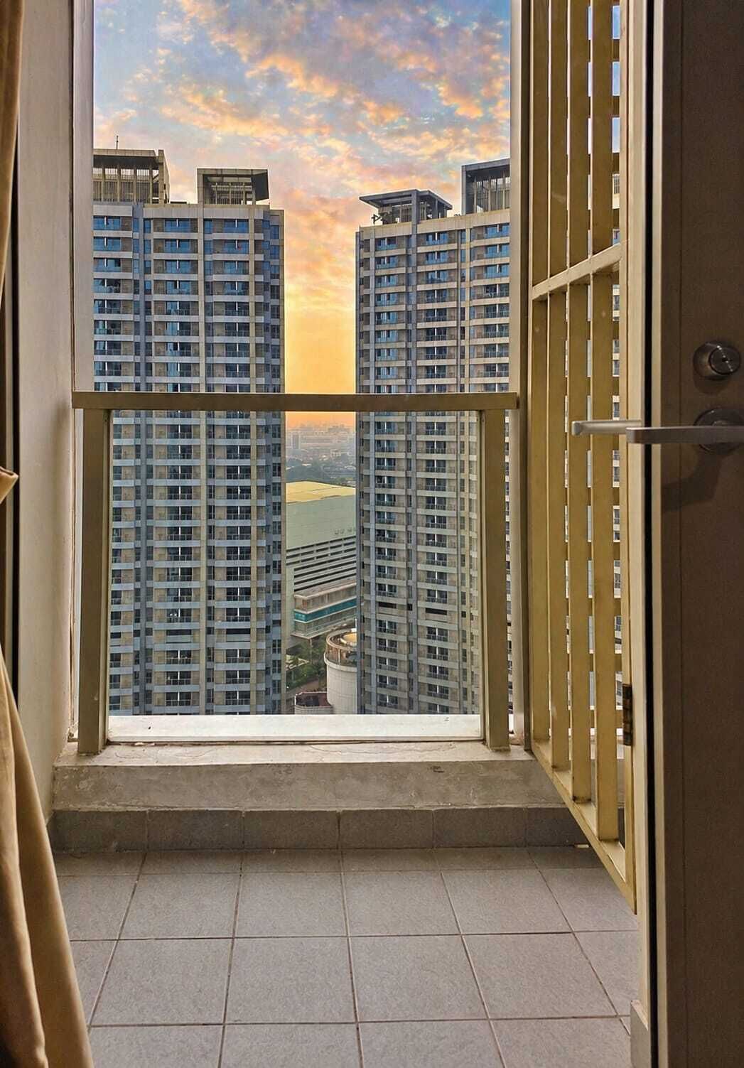 A balcony with a view of high-rise buildings and a sunset sky.