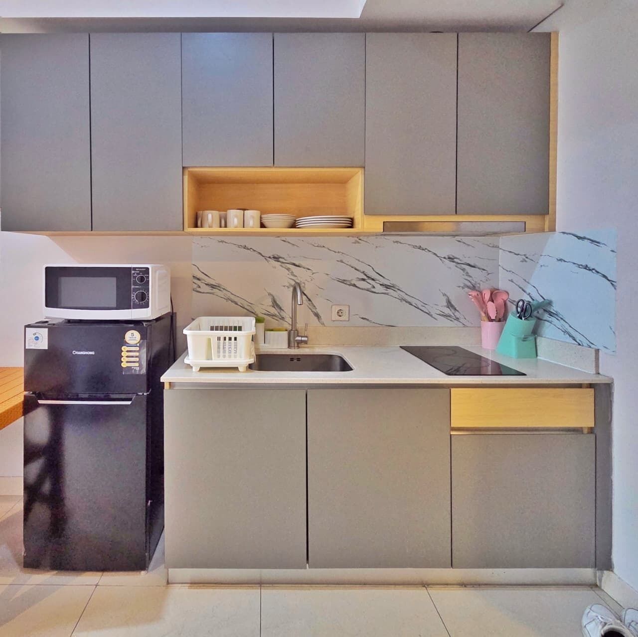 A modern kitchen with grey cabinets, a built-in microwave, a sink, and a countertop with a dish rack.