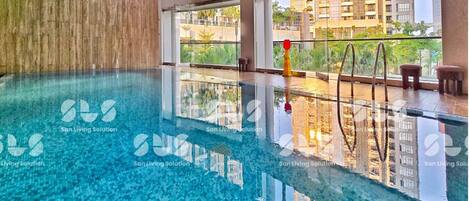 A modern indoor swimming pool with clear water, large windows, and a view of surrounding buildings.