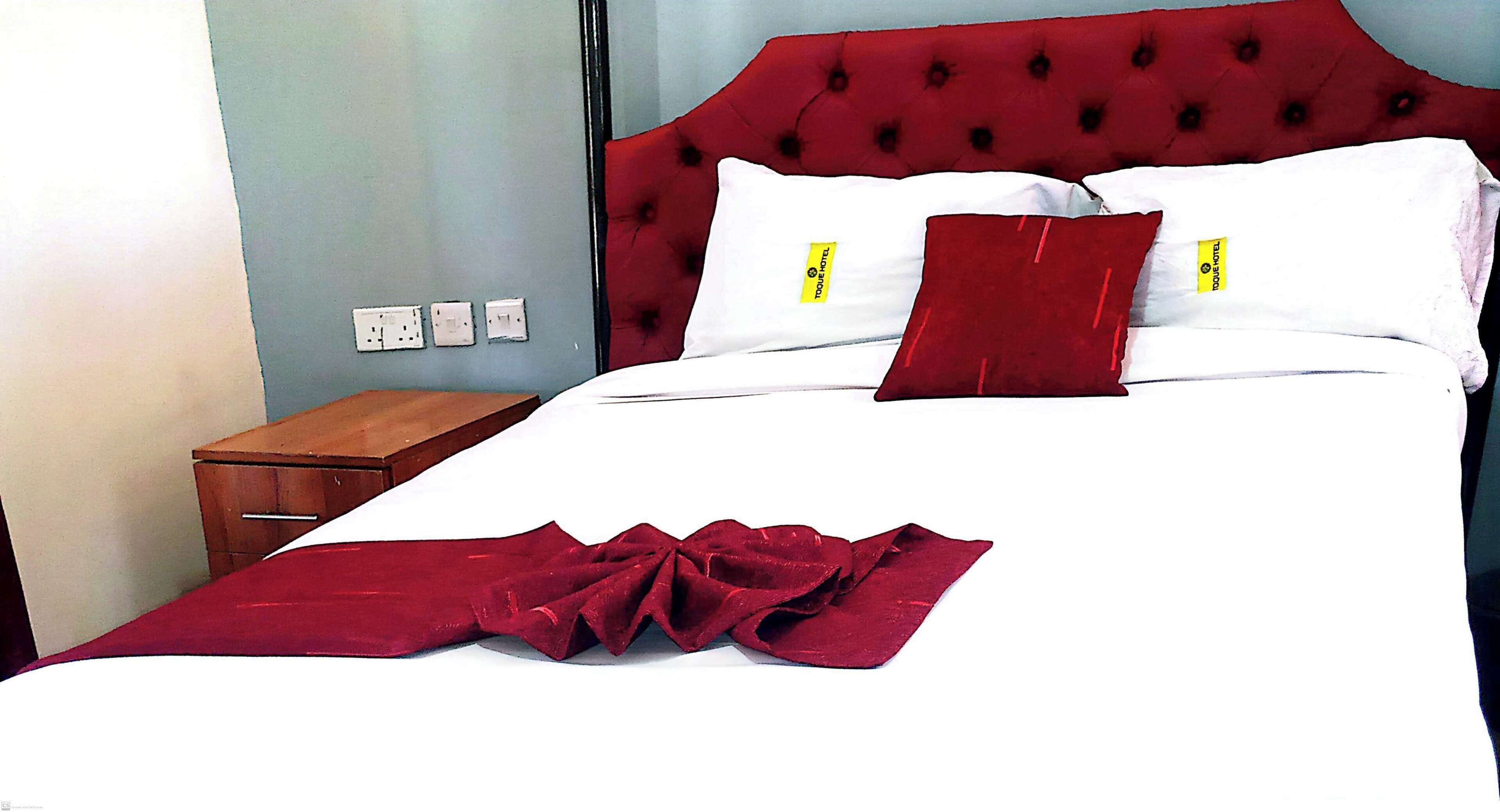 A hotel room with a red tufted headboard, white bedding, and a wooden nightstand.