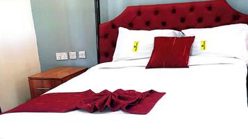 A hotel room with a red tufted headboard, white bedding, and a wooden nightstand.
