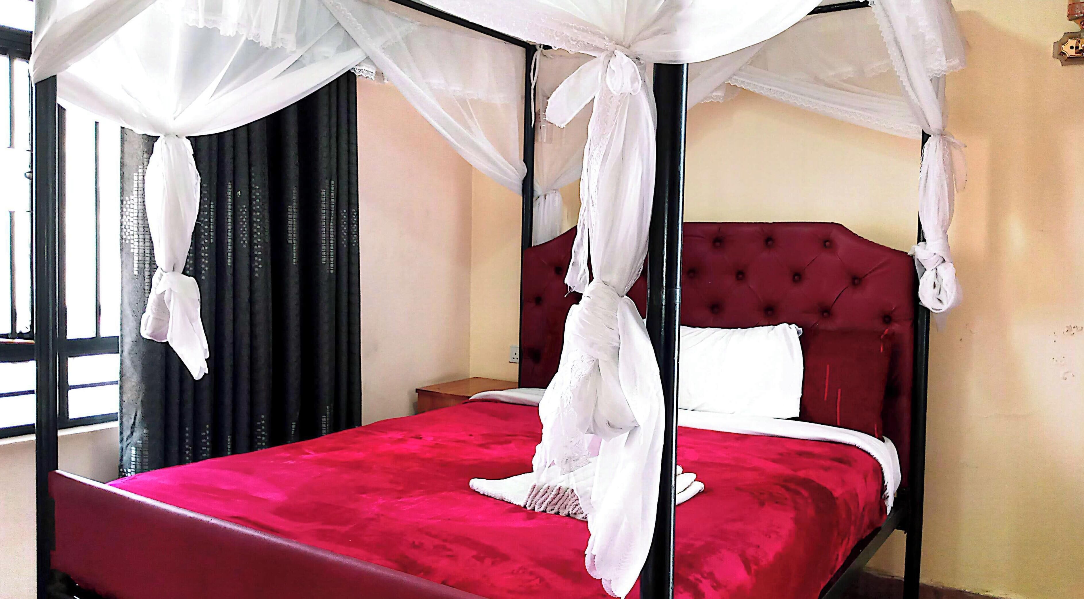 A bed with a red bedspread, a white canopy, and a red upholstered headboard.
