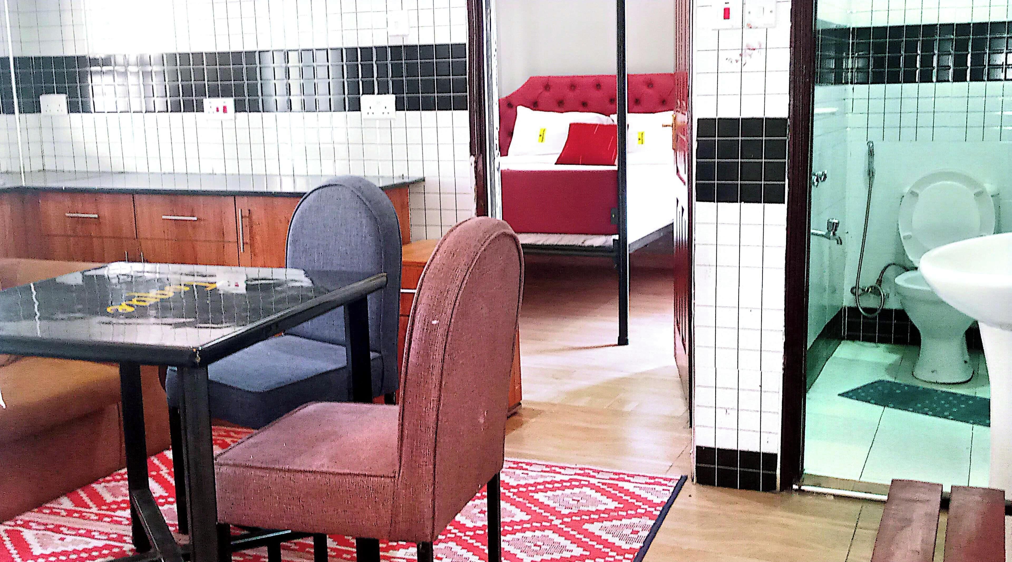 Une pièce comprenant une table à manger, un canapé rouge, un tapis à motifs, un mur recouvert de carreaux et une salle de bain avec des toilettes.