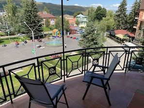 Un balcón con dos sillas, vista a un parque infantil y un edificio con techo rojo al fondo.