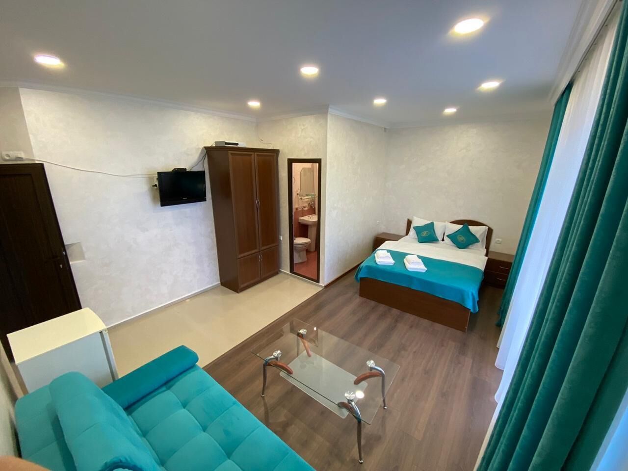 Une chambre d’hôtel de taille réduite, comprenant un lit, un canapé, une petite table, une armoire et un téléviseur.