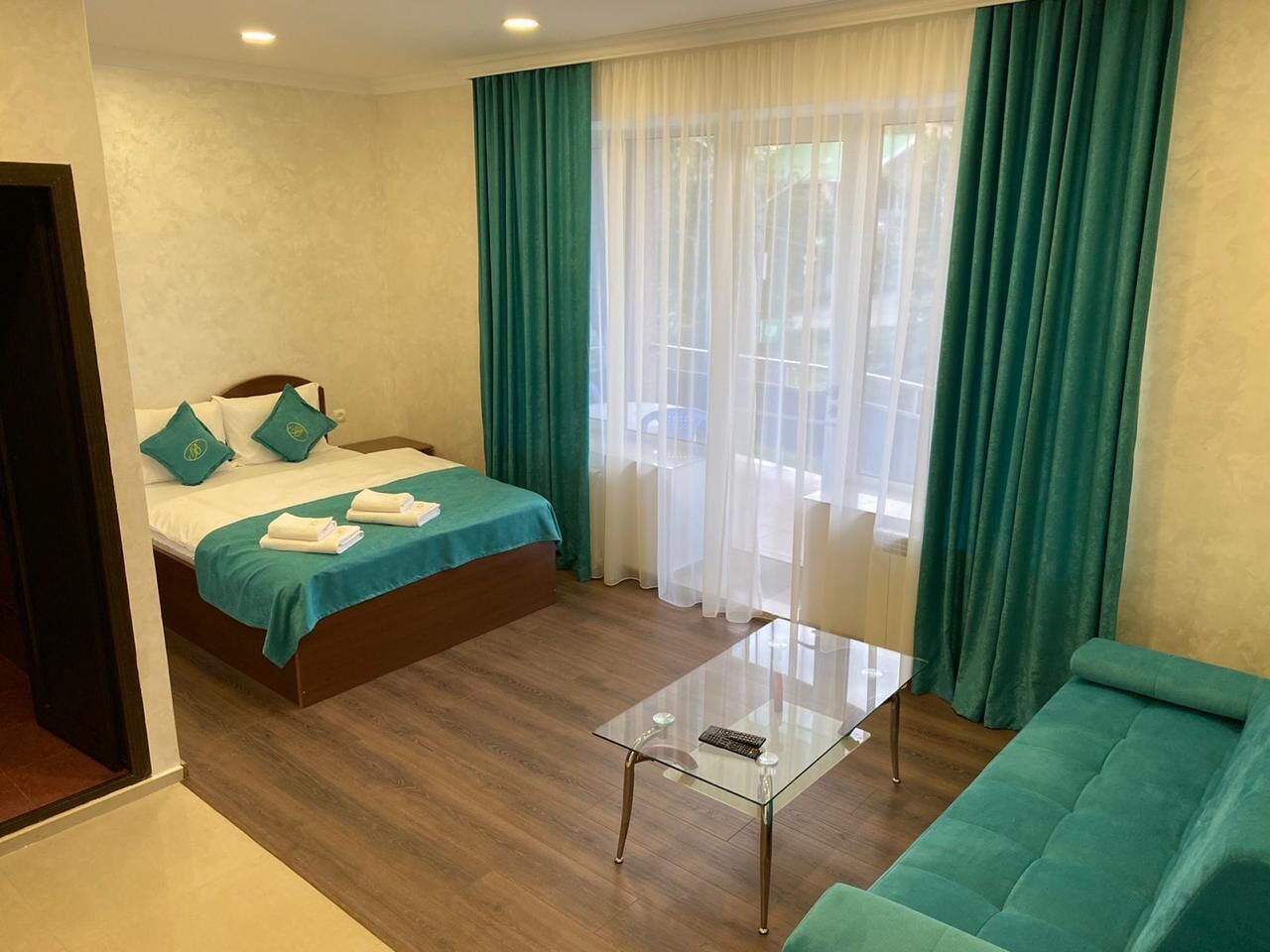 Une chambre d’hôtel avec un lit, une table basse en verre et un canapé vert.