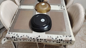 Une table à manger recouverte d’une nappe à motifs, entourée de quatre chaises de couleur beige.
