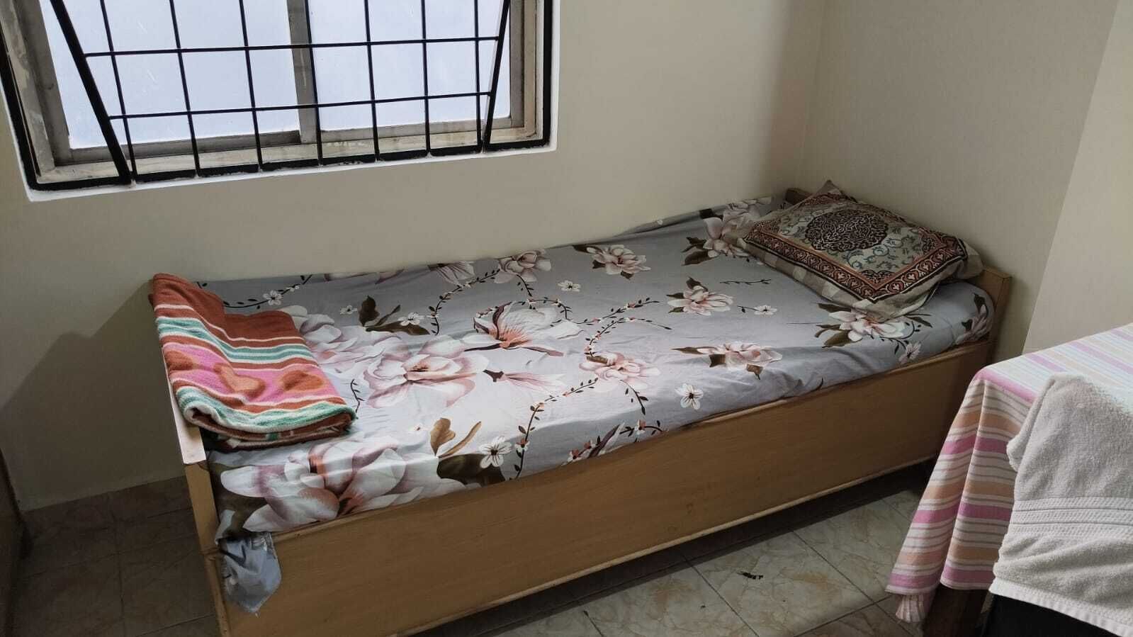 Una habitación pequeña con cama individual, una colcha estampada de flores, una manta a rayas y una almohada con diseño.