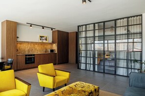 Ein modernes Wohnzimmer mit einer Küche, gelben Stühlen, einem gemusterten Hocker und einem großen Schiebeglasfenster mit Blick auf die Stadt.