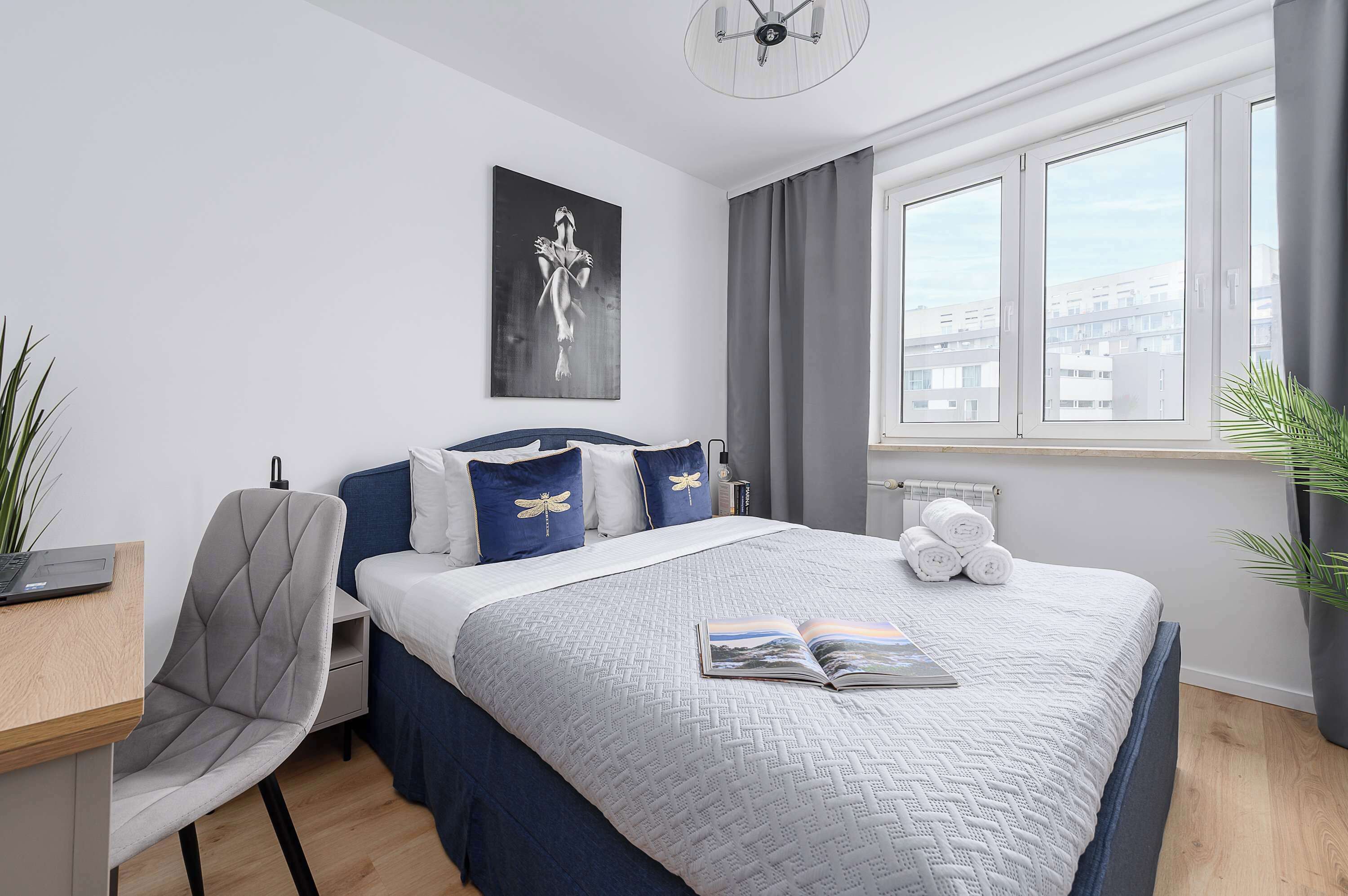 Ein modernes Schlafzimmer mit einem Bett, einem Sessel, einem Schreibtisch und einem Fenster mit Vorhängen.