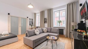 Een moderne woonkamer met een grijze modulaire bank, een klein rond salontafeltje en een aan de muur bevestigde televisie.