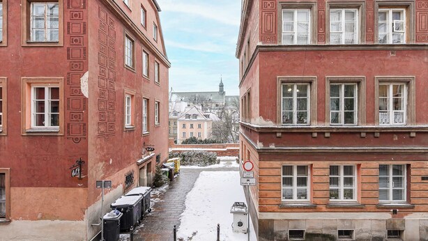Een smalle straat begrensd door rode bakstenen gebouwen met symmetrische raamontwerpen en een met sneeuw bedekte grond.