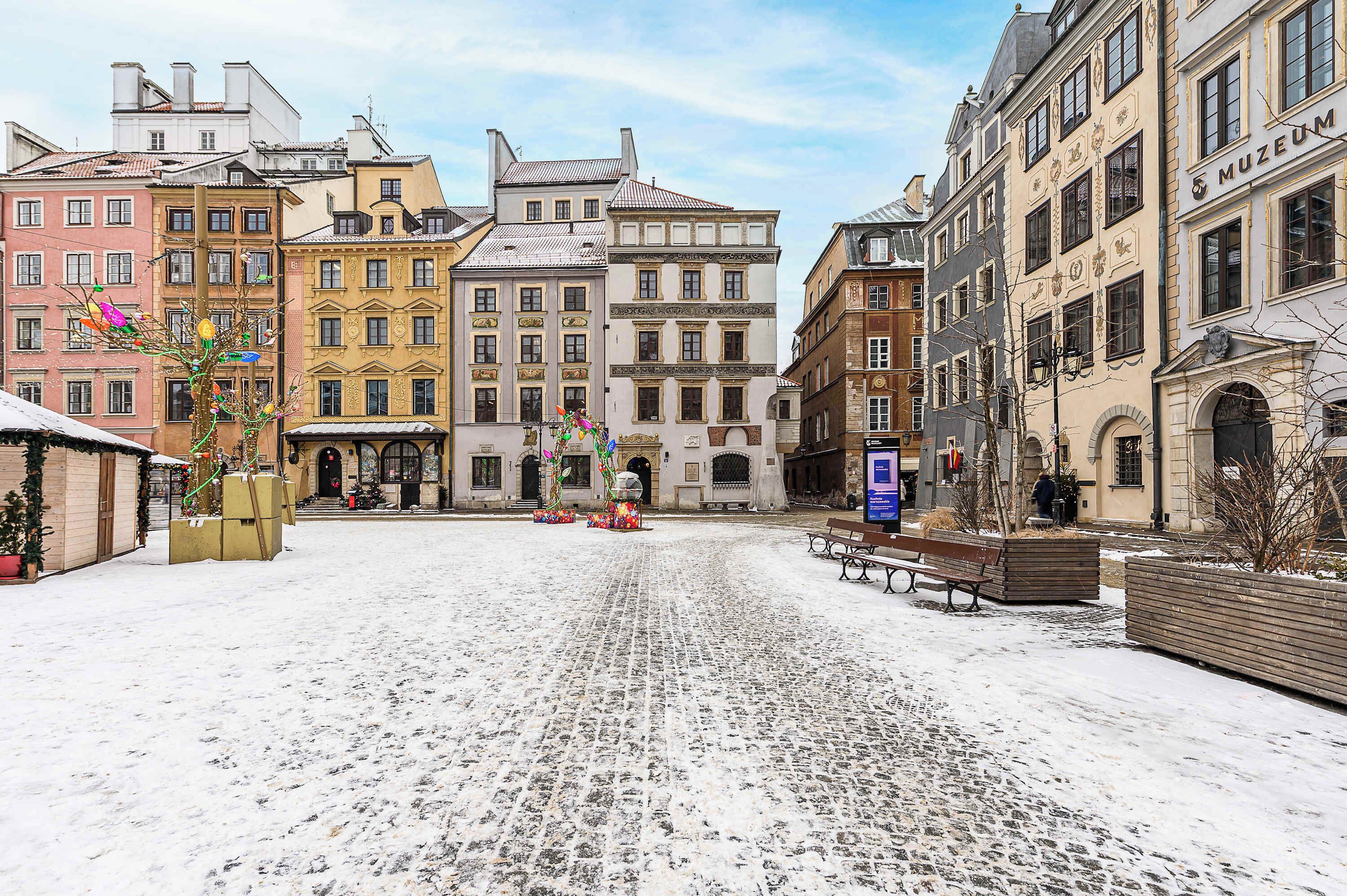 A cobblestone square with historic buildings, benches, and a snow-covered ground.