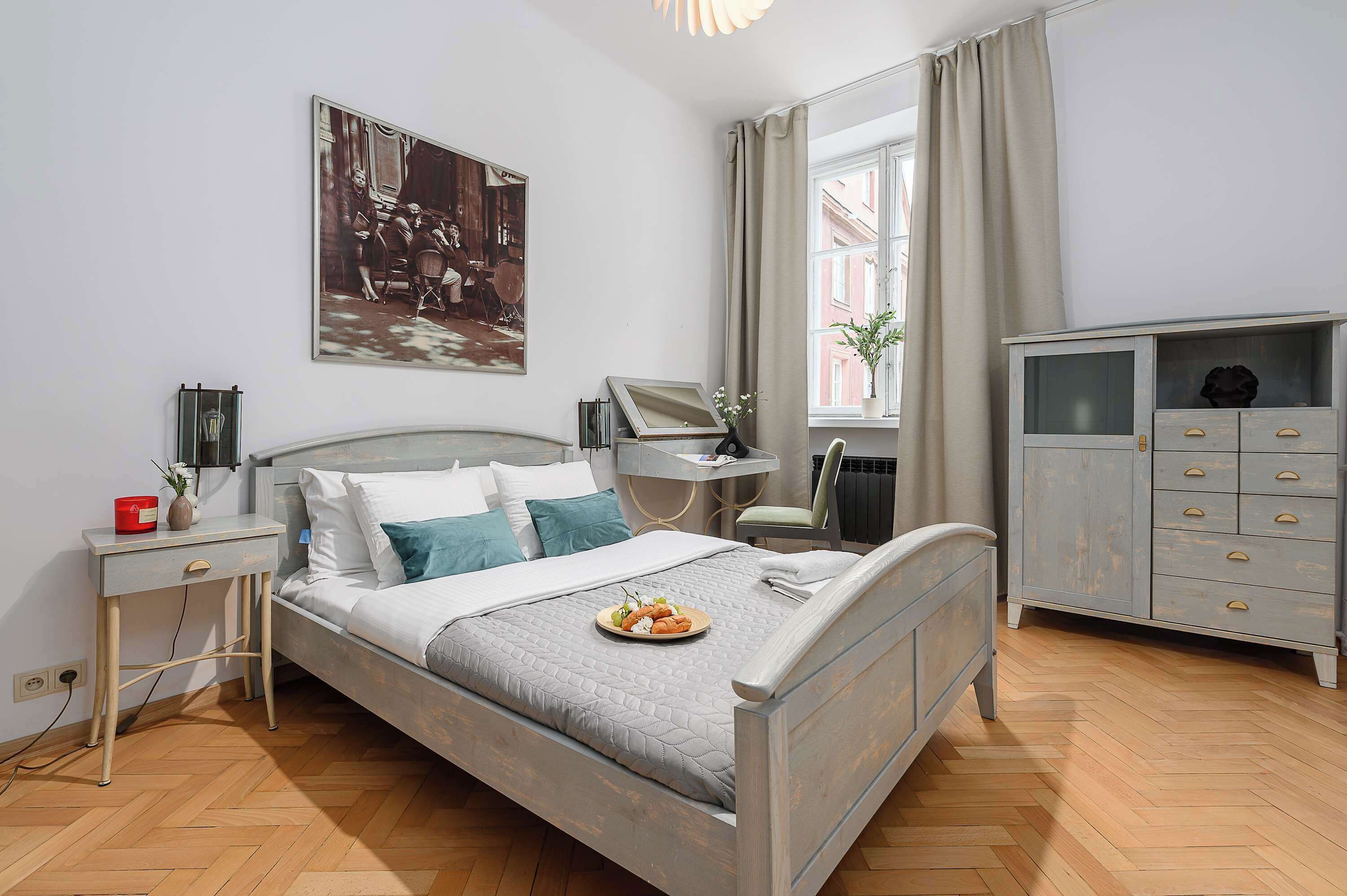 A neatly arranged bedroom with a bed, bedside tables, a dresser, and a window with curtains.