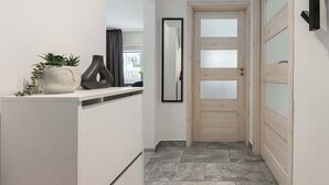 Un couloir avec une armoire blanche, un miroir et une porte en bois dotée de panneaux en verre dépoli.