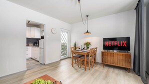 Un salon moderne avec un coin repas, une cuisine à l’arrière-plan et un téléviseur affichant le logo « NETFLIX ».