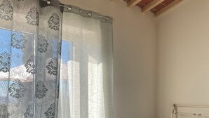 Ein Schlafzimmer mit einem Bett, einem Nachttisch, einer Lampe und einem Fenster mit Vorhang.