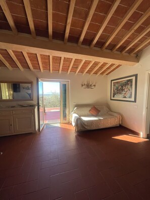 A spacious room with a high ceiling, a bed, a sofa, a dining table, and a view through a glass door.