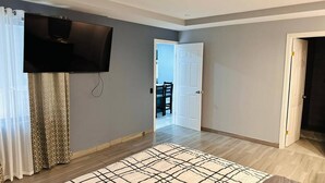 A room with a flat-screen TV mounted on the wall, a patterned rug on the floor, and a door leading to another room. - 3 bed 2 Bath 15 min From Airport (San Juan)