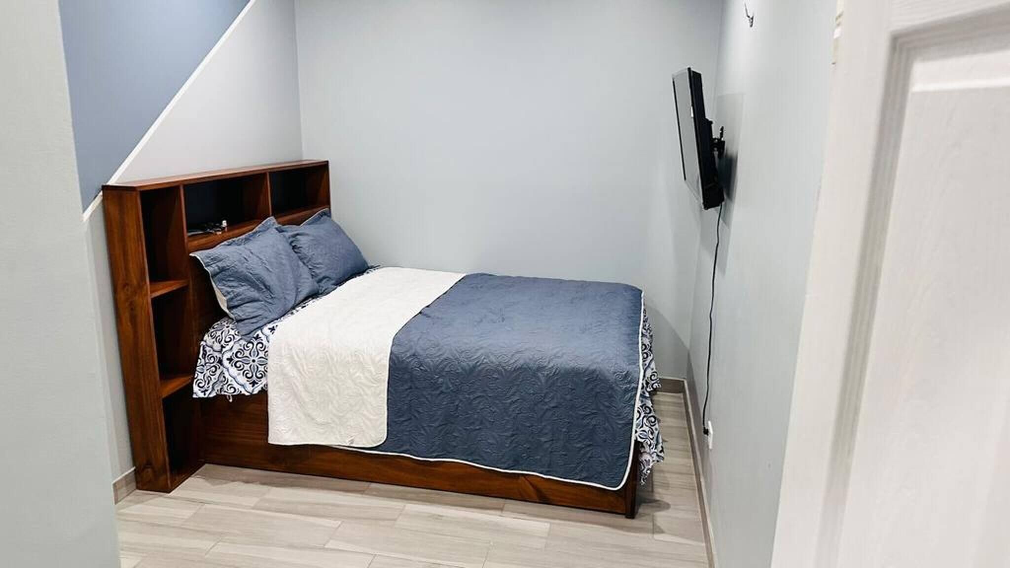 Ein kleines Schlafzimmer mit einem Bett, einer Holzregaleinheit und einem an der Wand befestigten Fernseher.