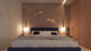 A modern bedroom with a striped wall, a dark headboard, two bedside lamps, and a bed with a striped bedspread. - Roches Marines (Saint-Paul)
