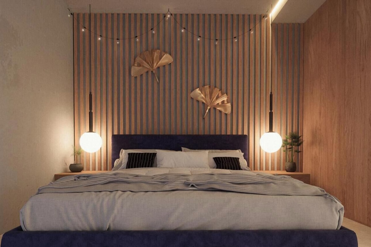 A modern bedroom with a striped wall, a dark headboard, two bedside lamps, and a bed with a striped bedspread.