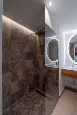 A modern bathroom with a glass-enclosed shower, a round mirror, and a wooden vanity.