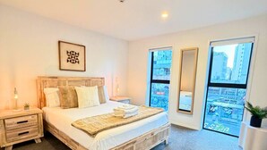 Un dormitorio moderno con una cama grande, una mesita de noche y una ventana con vistas a la ciudad.