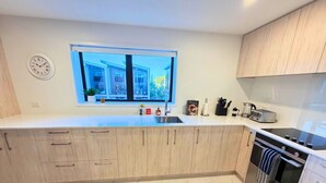 Una cocina moderna con armarios de madera, horno empotrado, lavamanos y ventana con vistas a la calle.