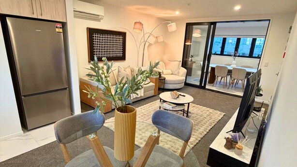 Una sala de estar moderna con una mesa de comedor de vidrio, sillas tapizadas de color gris, un sofá y un ventanal con vistas.