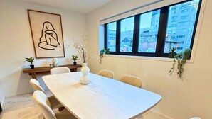 Un moderno comedor con una mesa rectangular, seis sillas, un florero con ramas y una obra de arte enmarcada en la pared.