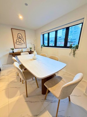 A modern dining area with a rectangular table, six chairs, a vase with branches, and a framed artwork on the wall. - Serene Getaway - 2BR on Manchester Street (Christchurch)