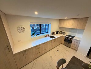 A modern kitchen with a large window, wooden cabinets, a built-in oven, and a clock on the wall. - Serene Getaway - 2BR on Manchester Street (Christchurch)