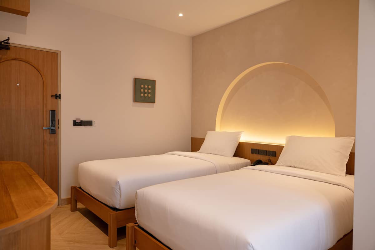 A hotel room with two beds, a wooden desk, and a wall-mounted light fixture.