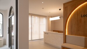 A reception area with a reception desk, a wooden accent wall, and a large window. - Taupe Hotel (Chiang Mai)