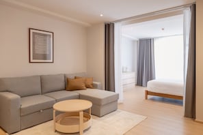 A modern living room with a grey sofa, a round coffee table, and a bed with a wooden frame. - Taupe Hotel (Chiang Mai)
