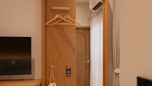 A hotel room with a wooden door, a TV on a stand, a hanging bag, and a mirror. - Taupe Hotel (Chiang Mai)