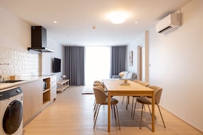A modern kitchen with a washing machine, a dining area with a table and chairs, and a living space with a sofa and a TV. - Taupe Hotel (Chiang Mai)