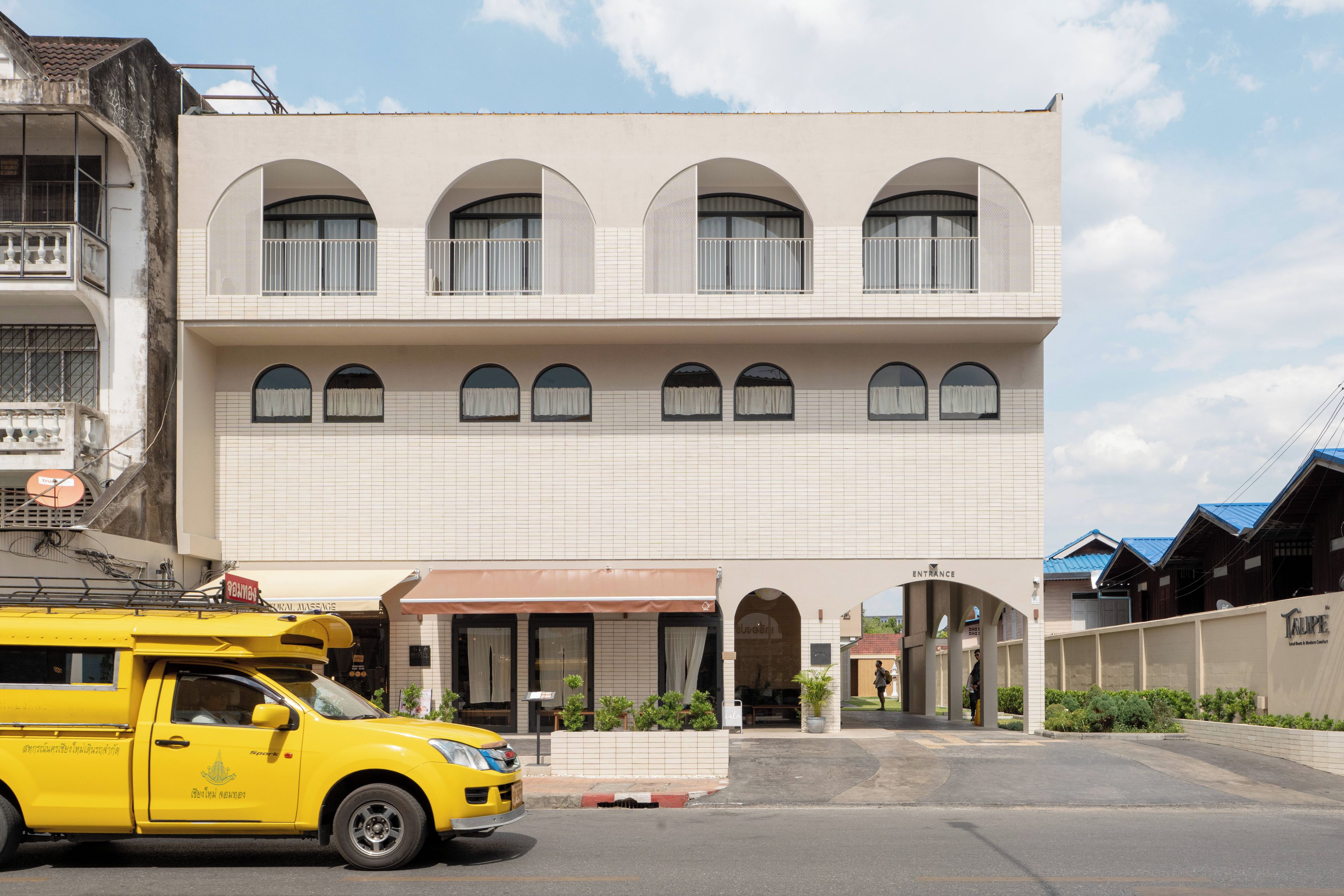 Een gebouw met twee verdiepingen, een centrale ingang, meerdere ramen en een gele taxi ervoor geparkeerd.